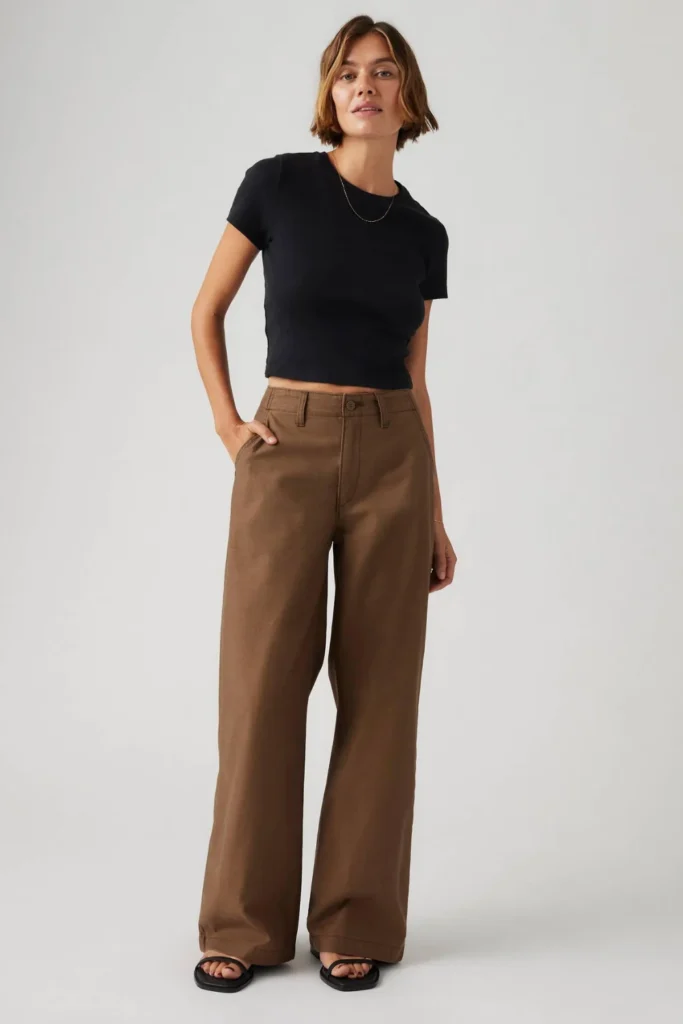 Woman styling brown jeans with a black t-shirt and white sneakers for a modern casual look