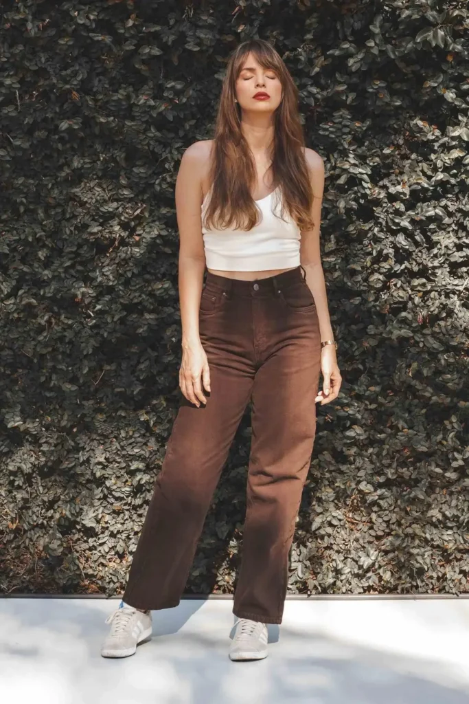 Woman wearing high-waisted brown jeans with a neutral crop top and sneakers for a summer outfit
