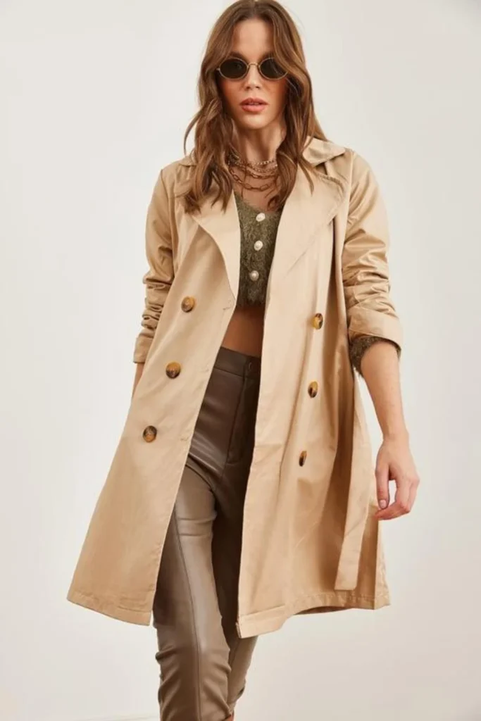 Woman wearing brown jeans with a beige trench coat, white sweater, and ankle boots