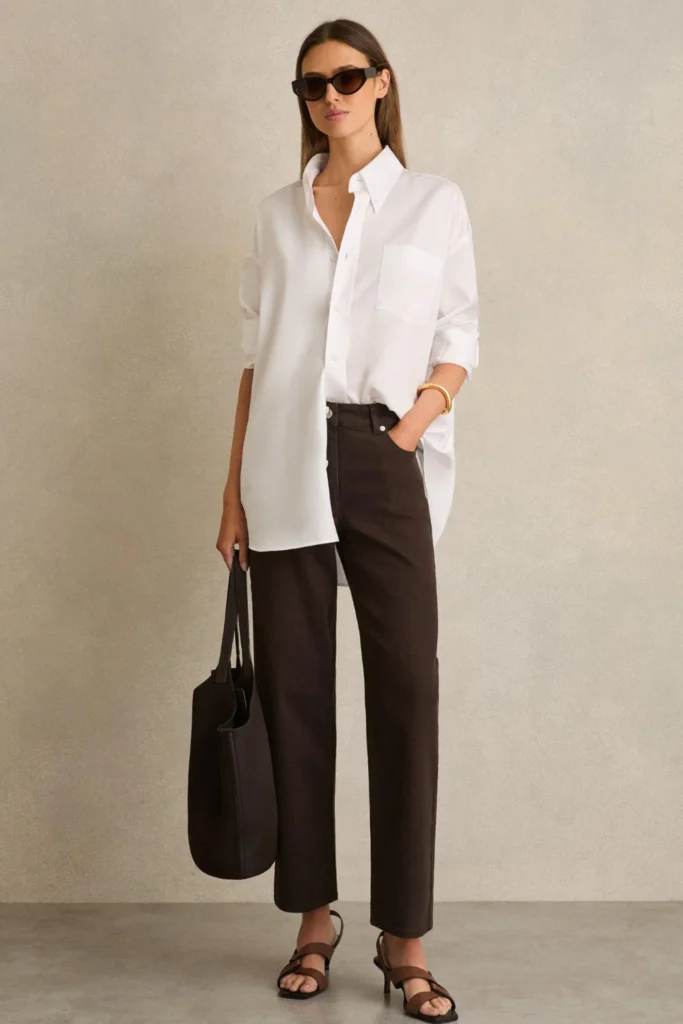 Woman wearing brown jeans with a white button-down shirt and sneakers for a casual outfit