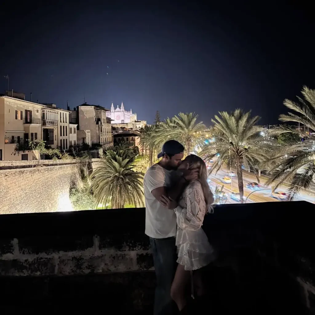 Sydney Sweeney kissing a man on a balcony at night during a summer getaway.
