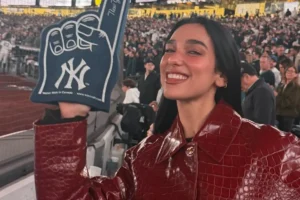 Dua Lipa wearing a burgundy leather coat and holding a New York Yankees foam finger at her first baseball game