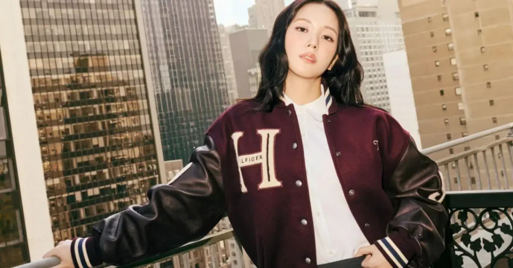 Jisoo wearing a burgundy varsity jacket with a gray pleated skirt