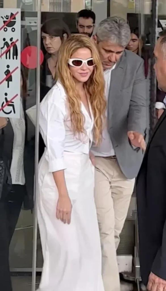 Shakira wearing white outfit and white sunglasses with security guard